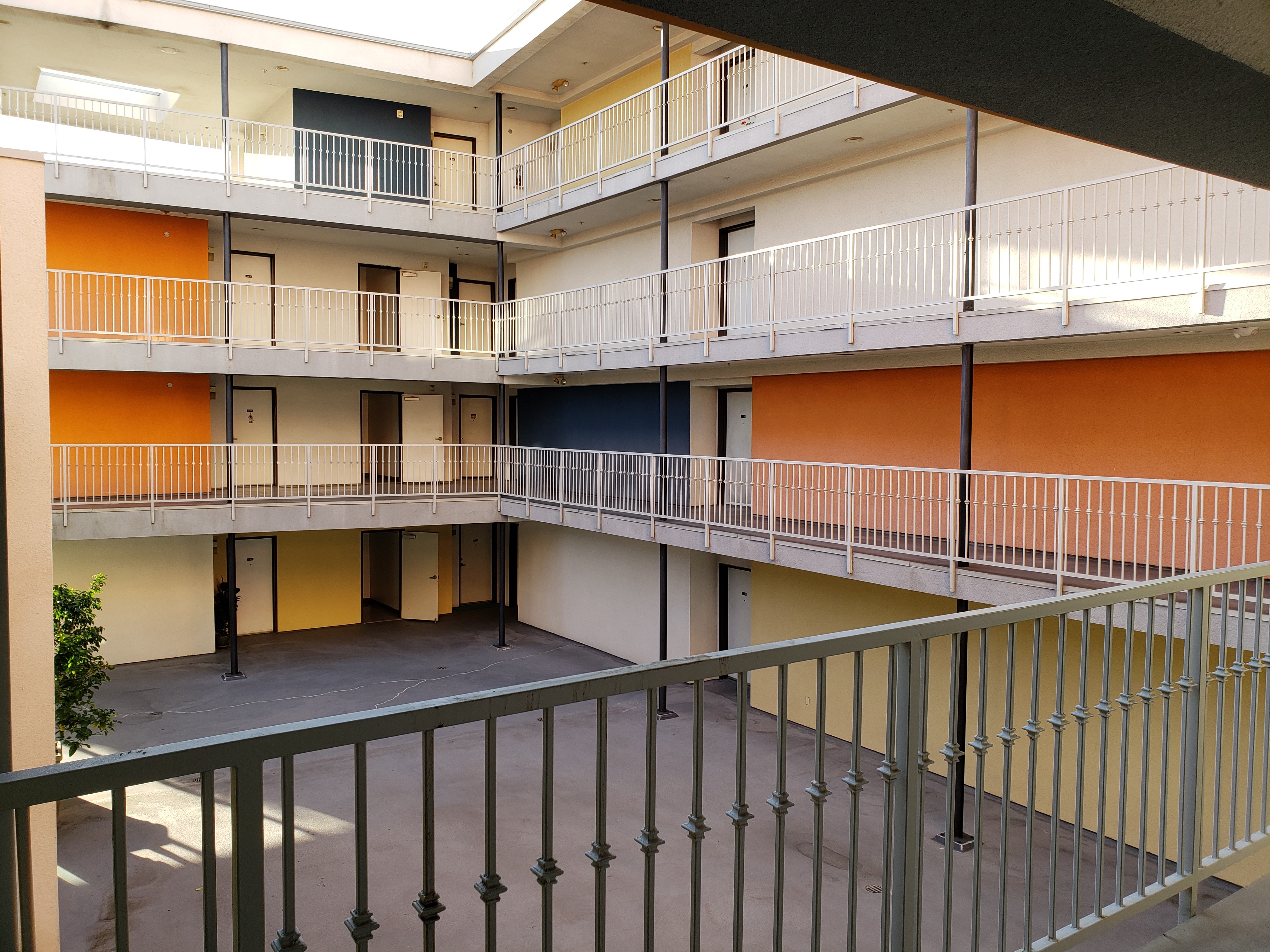 Inner view of a fourt story building. Pictured is an open central space and outter passageways to units on each floor. Small white fences are aligned on the outter section of the passageways.