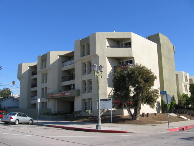 Corner view of 4 floor, tan building with balconies and street parking