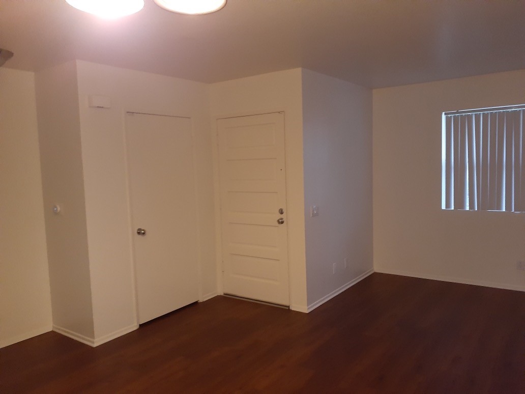 View of a empty unit, main entrance door, a second door, white walls, brown laminate floors.