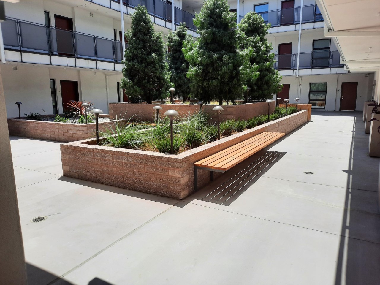 Outdoor patio area located at the center of the building. There are four trees, surrounded by planters, plants, and lamps with benches and trashcans available.