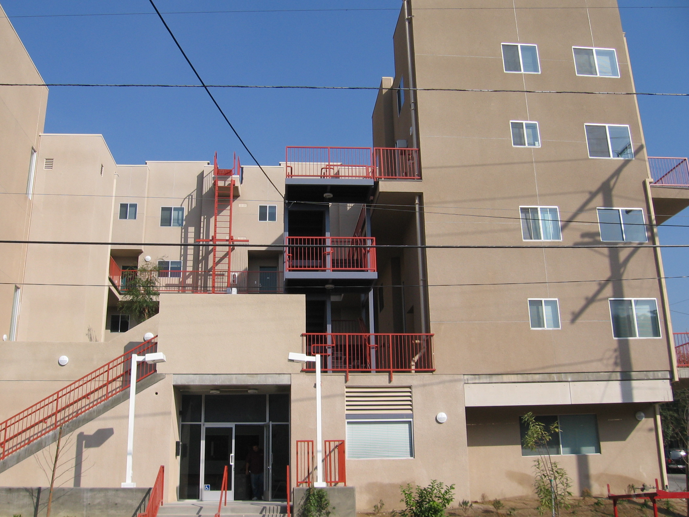 Front view of a three story brown building with red railings and stairs at the front entrance