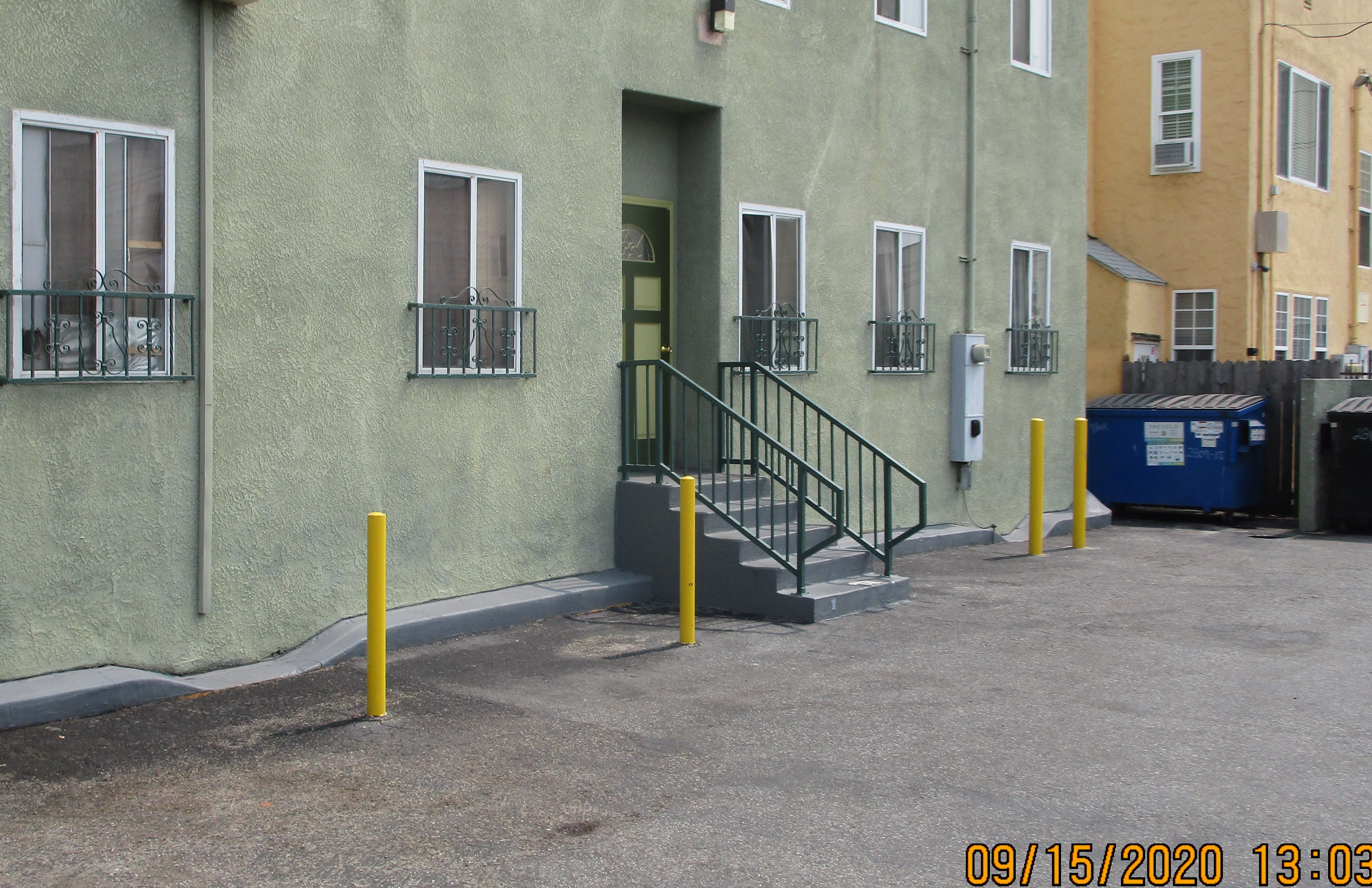 Image of the building entrance with stairs, windows on both sides of the entrance, and vertical yellow parking poles.