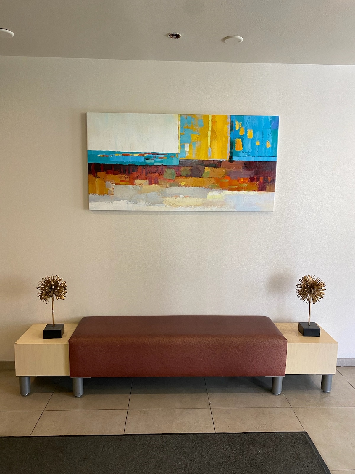 Lobby area with a bench and a multicolored painting on the wall.
