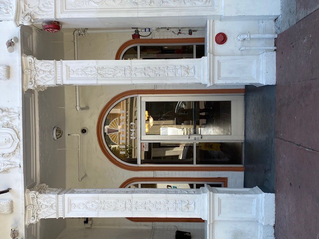 View of the entry way of the Bellevue Apartments, white ornate pillars lead to the single glass door entry with long windows on both sides
