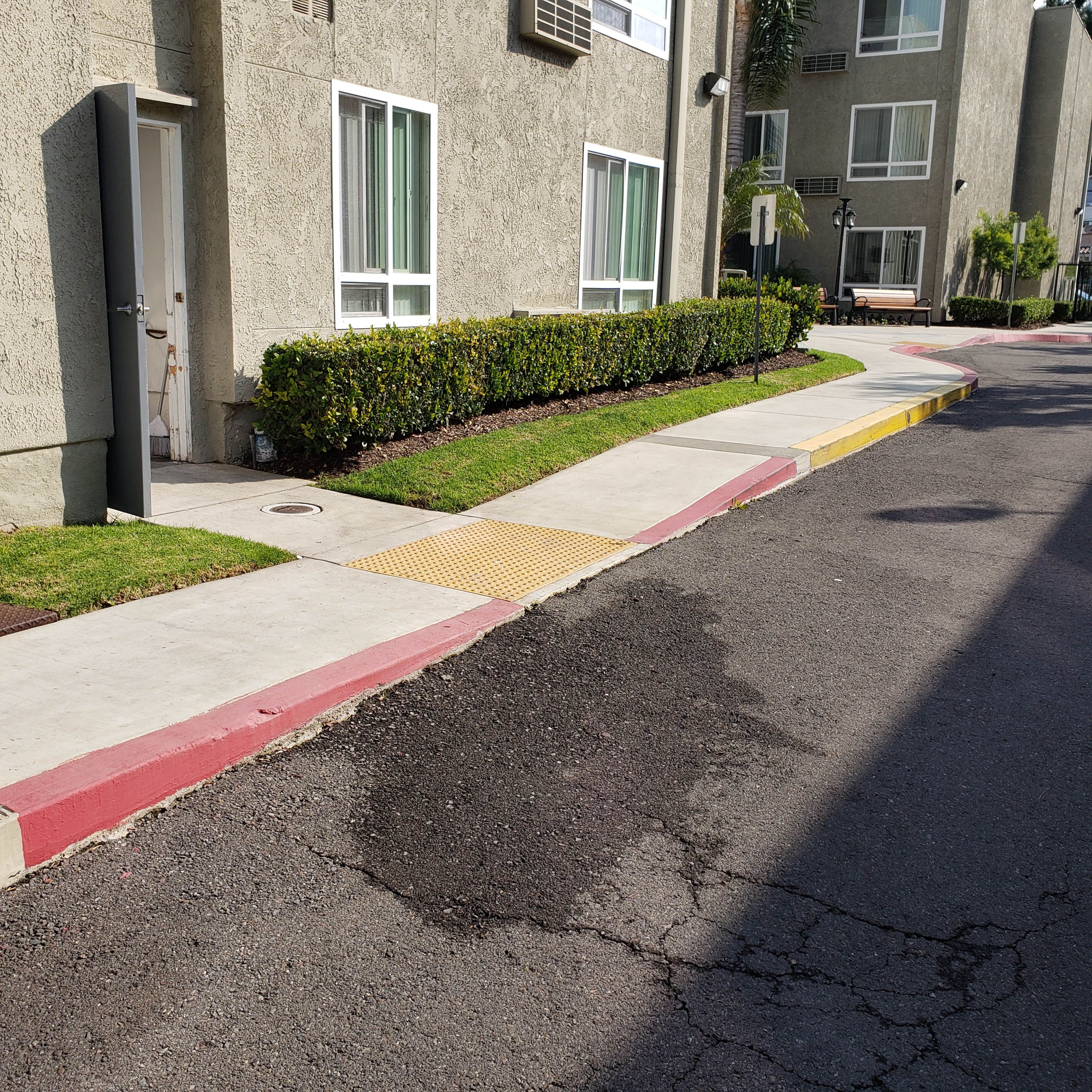 Image of tres lomas garden apartments travel path. building lined with bushes/ curbside painted red with accessible path into building