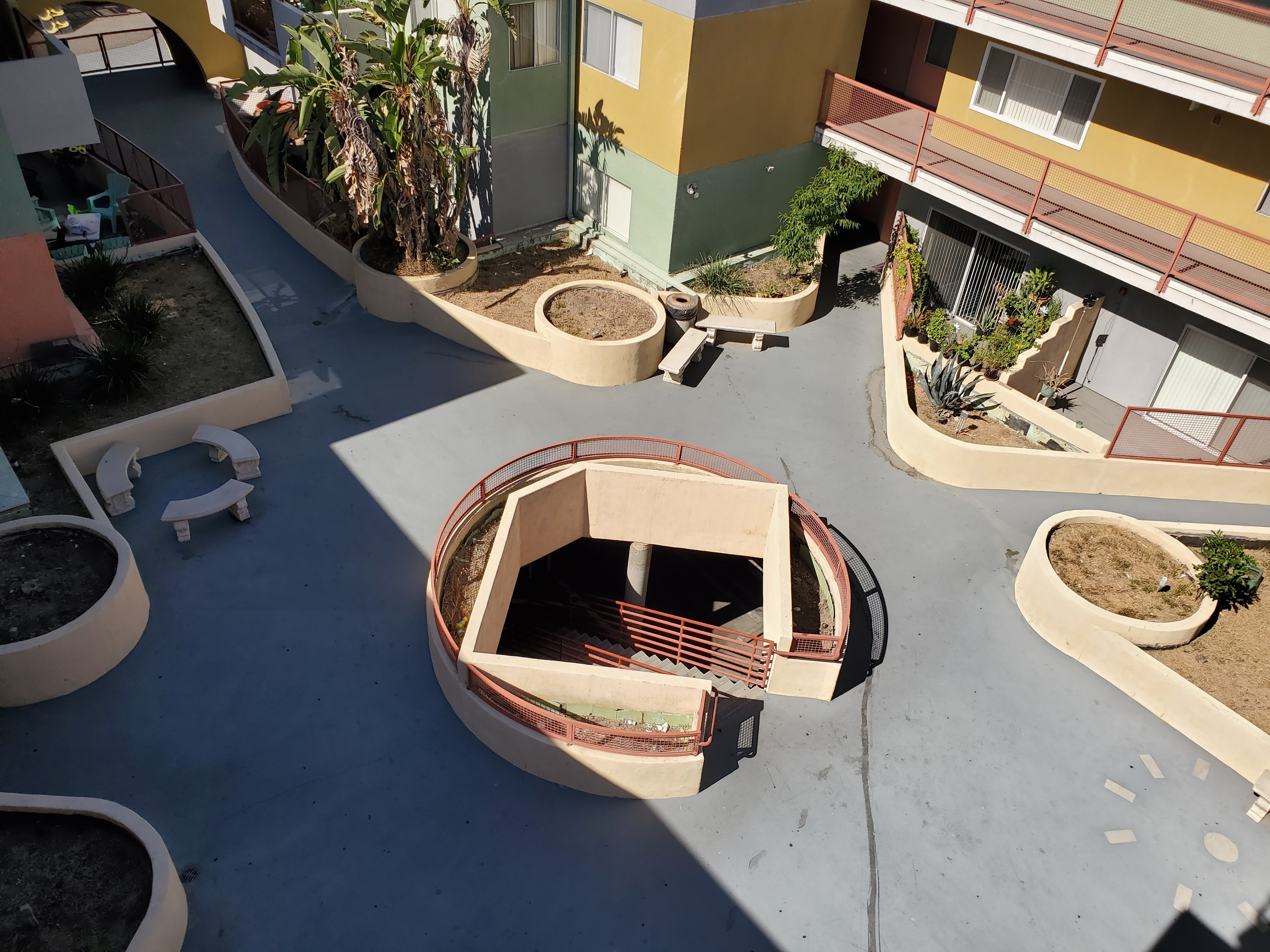 View of a patio, courtyard style, concrete benches, a round spiral stairs in the middle with handrails, plants around.