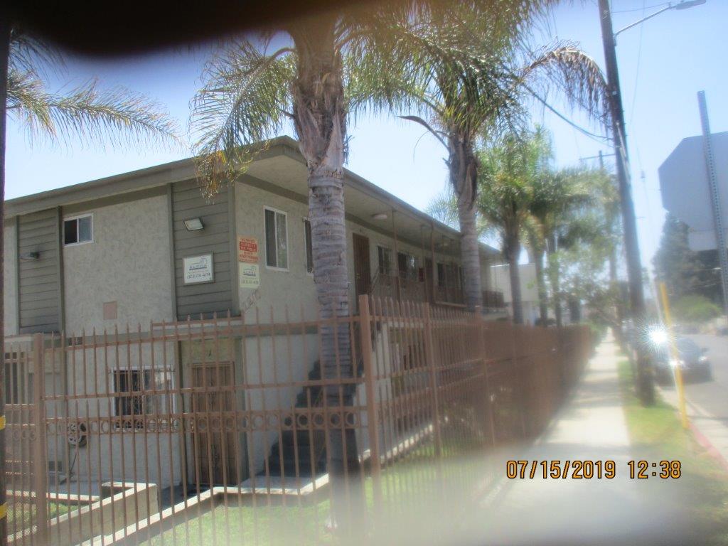 Side view, two story building, gated, palm trees along the building, multiple windows, iron screen doors, stairway up to the second floor with handrails, ligh lamps and no public parking and management company signs.