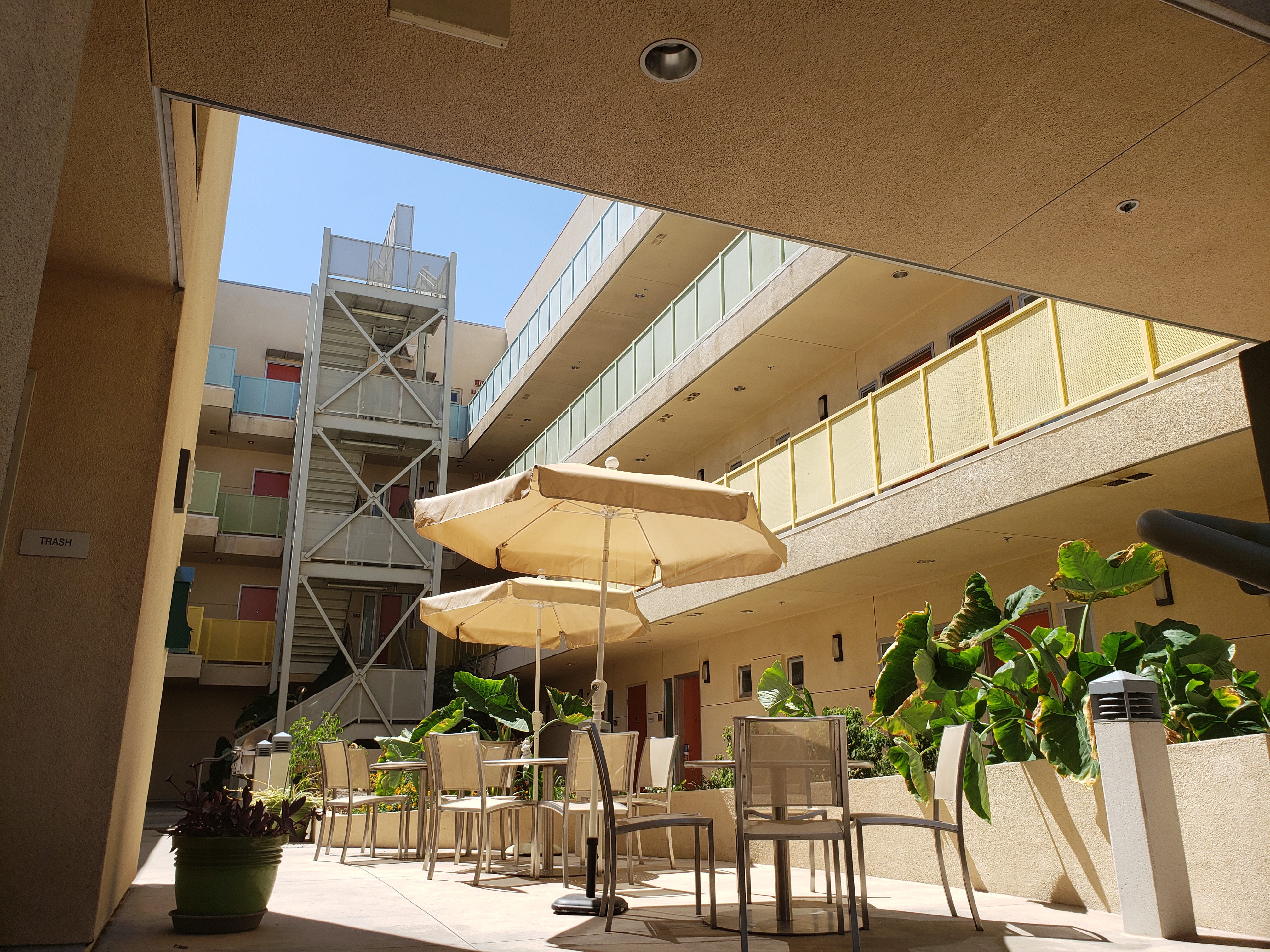 patio view. patio tables with umbrellas and chairs centered 
in the middle of three story building. Planters along side 
seating area. View of stairs on the far end of seating area