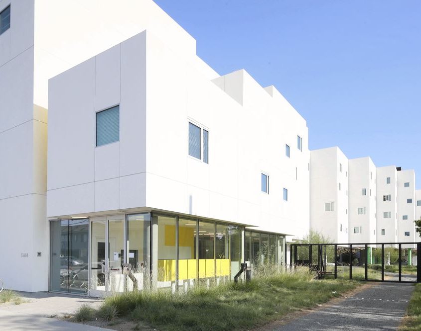 Exterior front view of Crest Apartments. All white building with yellow trim inside that you can see through floor length windows on the first floor.