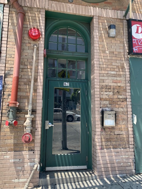 Green door entry, building number on top of the door, call box on the right side, barrel fire hydrants on the left side, light lapm on the right side.