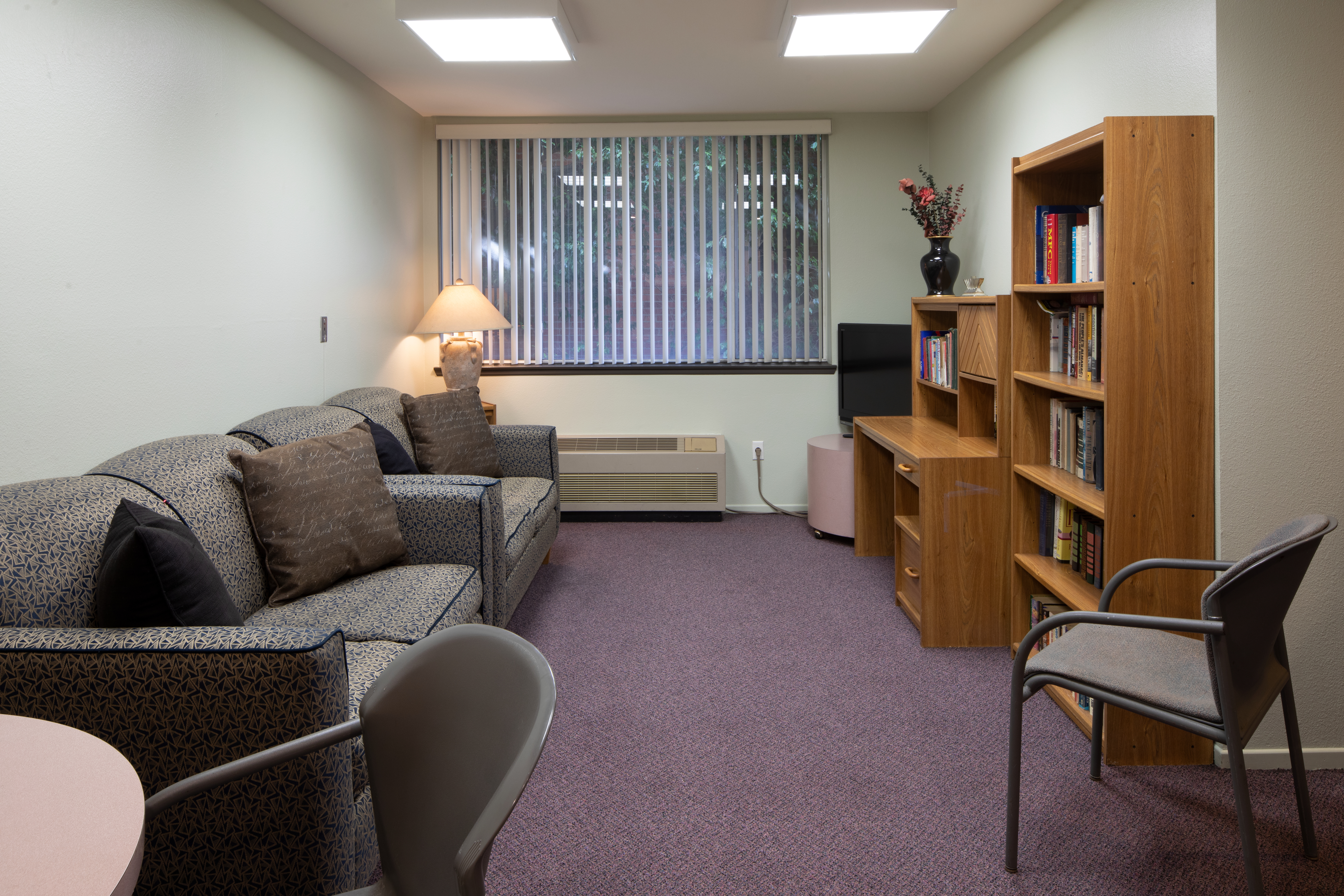 Interior view of a community room at Miracle Mile with couches, chairs, a television and bookcase.