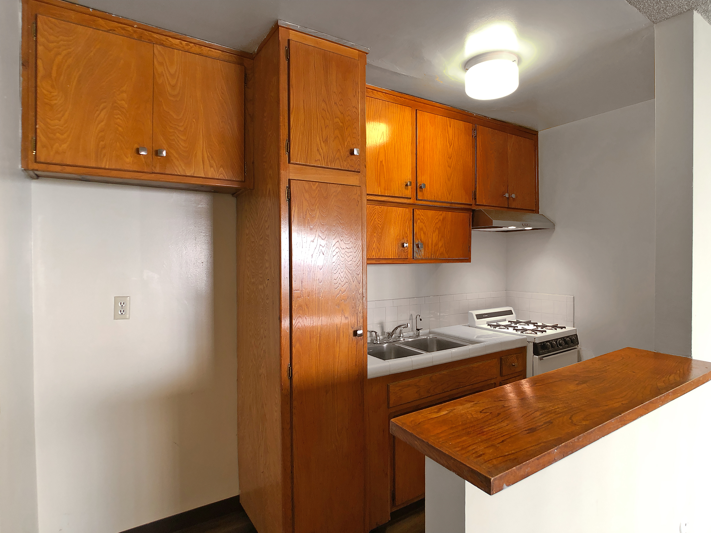 Photo of kitchen showing sink, kitchen cabinets, sink, countertop, stove and empty space for fridge