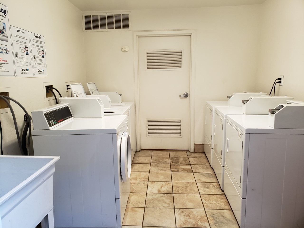 Laundry room with six machines that are across each other. Walls have posted signs.