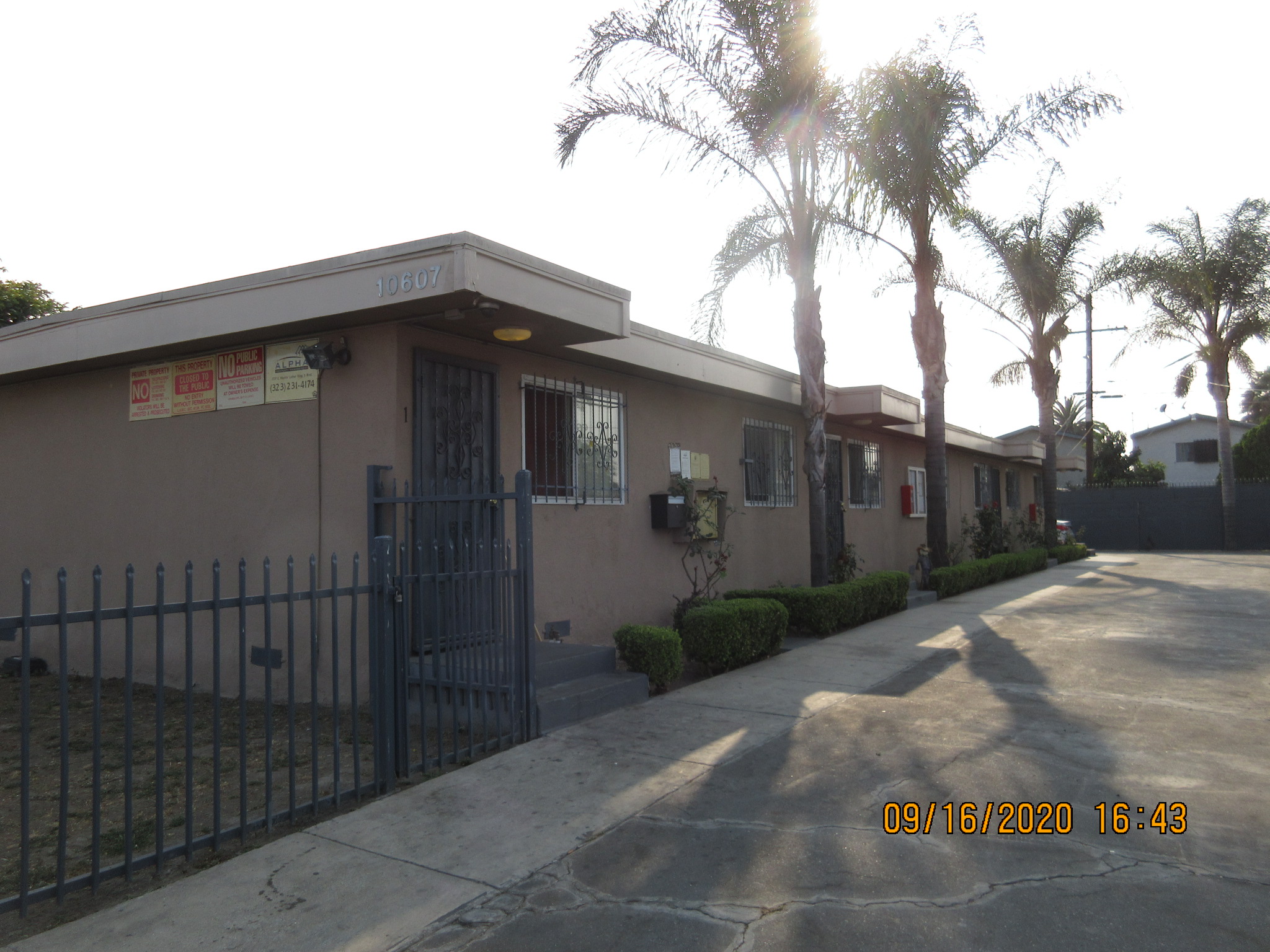 Side view of a brown and beige three units next to each other, all windows gated, iron screen doors, no public parking and management company signs, light lamps, palm trees and middle size bushes right in front of the units.