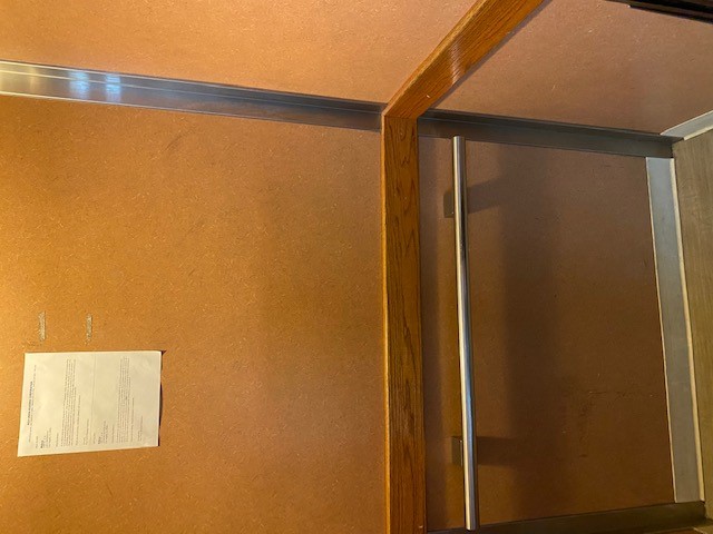 Inside view of an elevator with a metal horizontal grab bar and a posted sign on the wall.