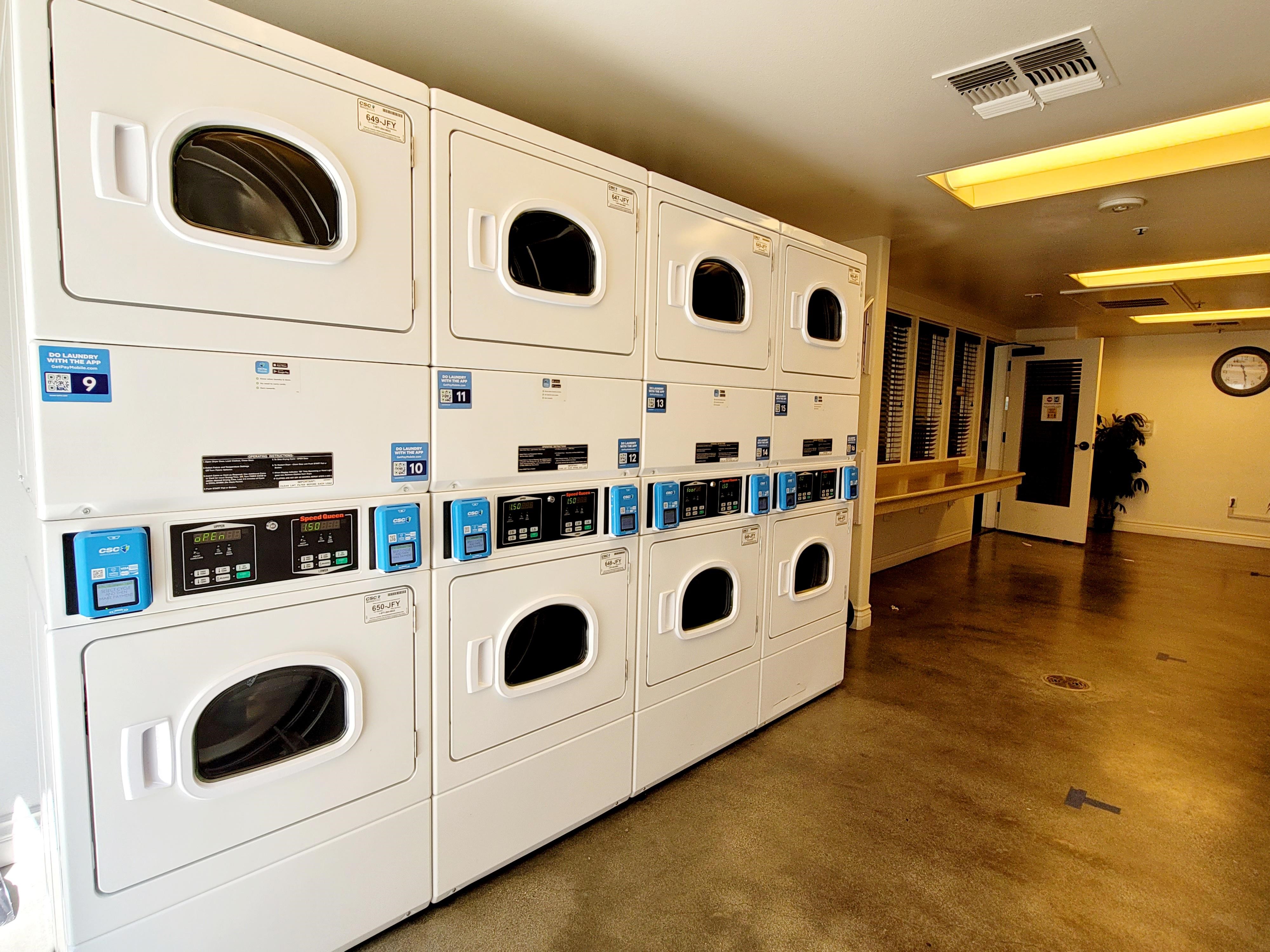 Del Rey Square Senior Housing laundry area. Stacked dryer machines along wall. Long folding table located next to dryers.