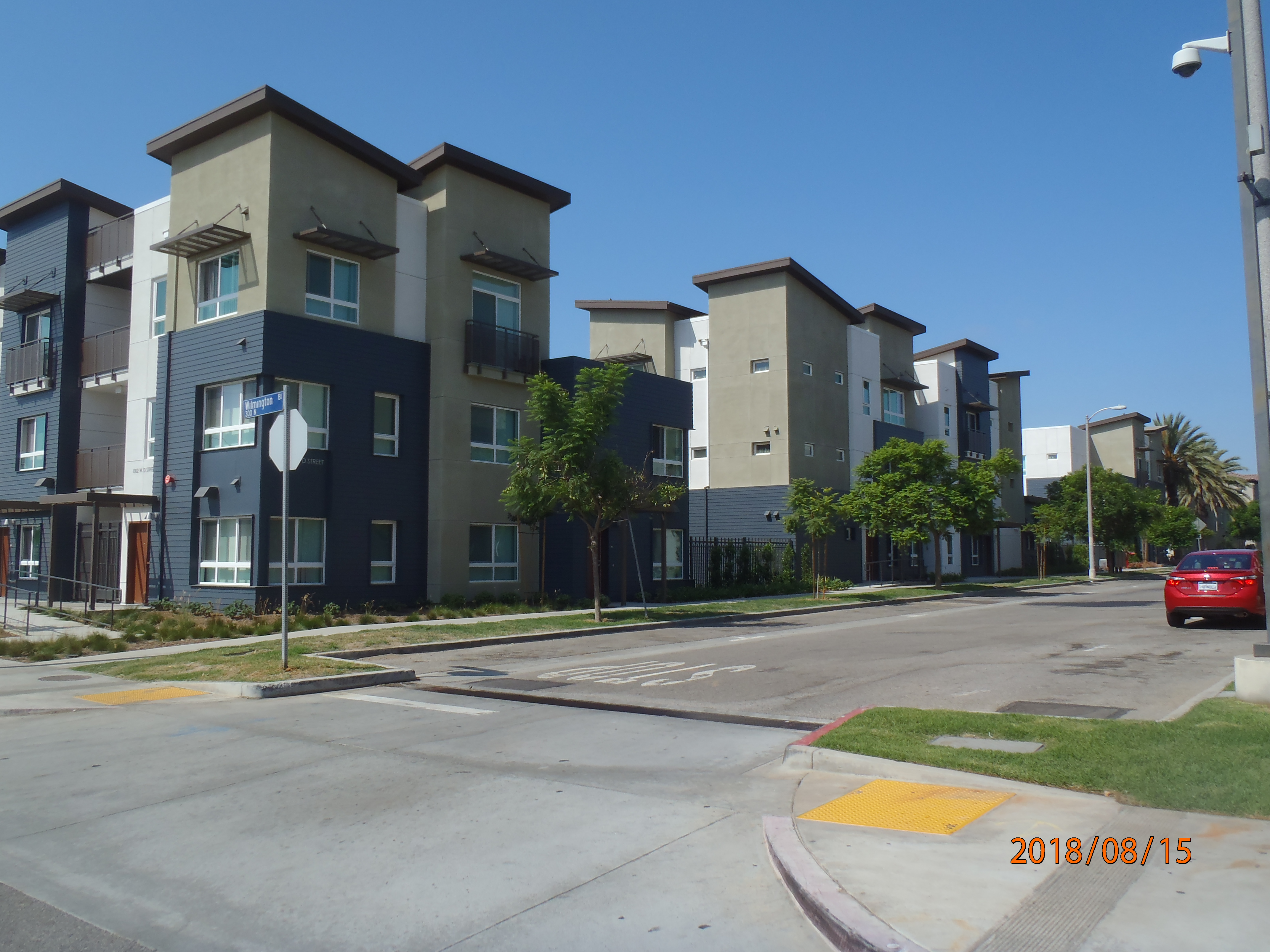 Three story blue, olive green, and white colored modern building. Entry way has ramp access. Newly planted foliage surrounds the building.