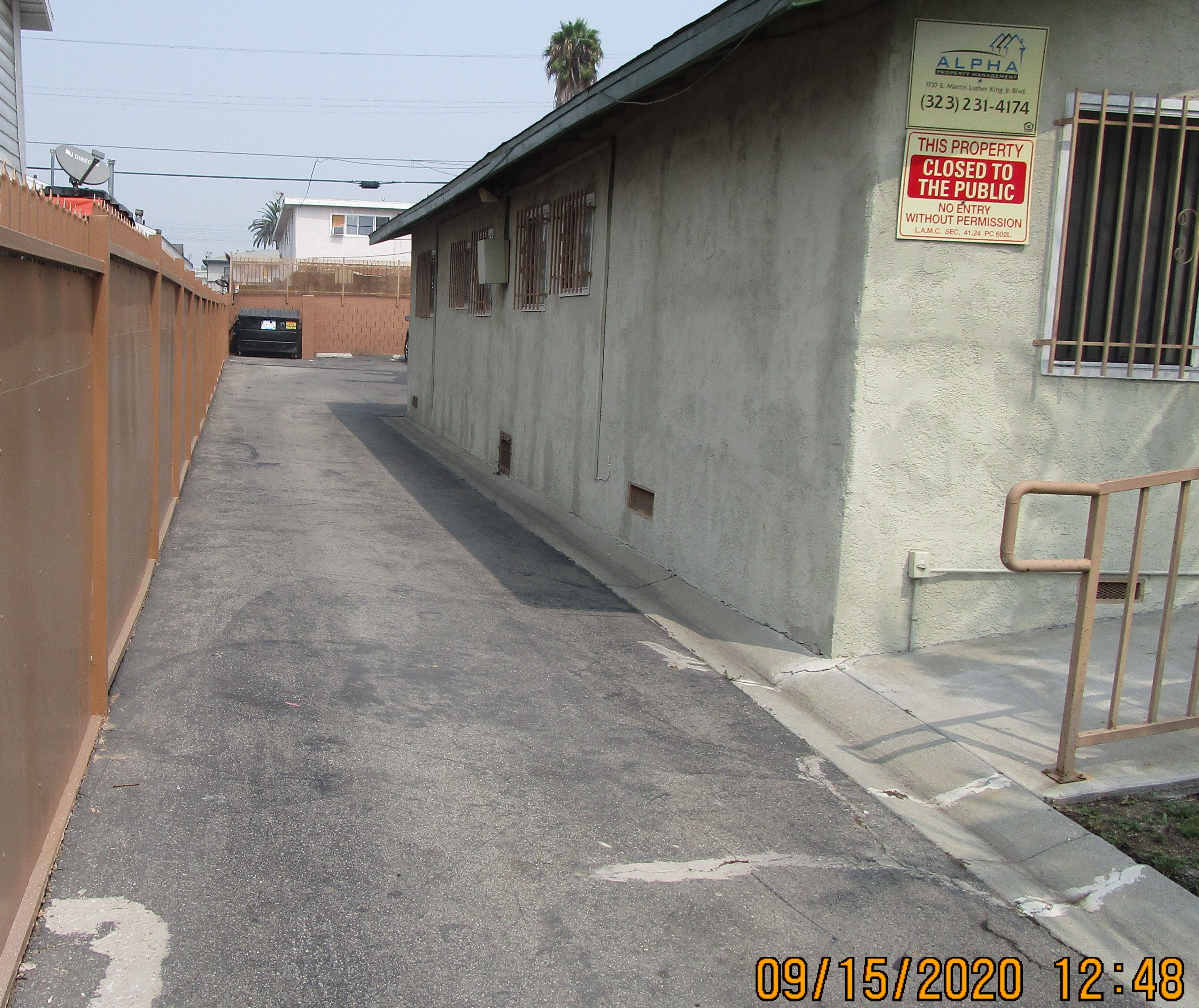 Front view of an open entrance to the parking, concrete, big brown trash bin against the wall at the end.