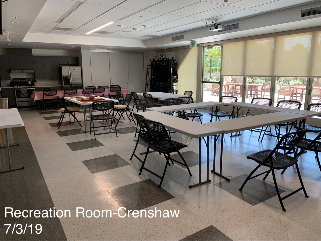 Interior view of Durae Crenshaw Apartments. The community kitchen/recreation room with a stove, refrigerator, white tables, back chairs and a view of the courtyard.