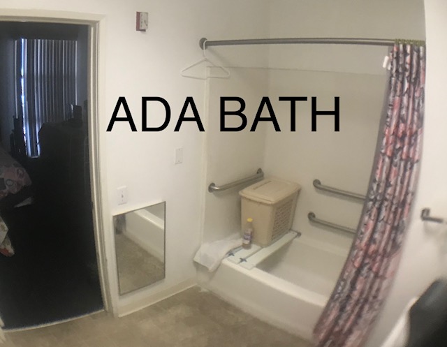 Image of bathroom in unit with seat and bar handles in bathtub area and mirror low to ground