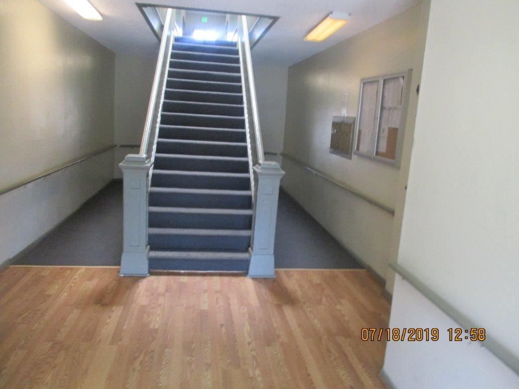 17 rugged staircase with strong wood handrails, lighted hall, half rug and other half laminate floor, to the right side a locked showcase and next to it the mailboxes.