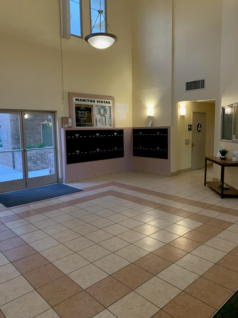 Lobby area with tile flooring. Mailboxes are located here. There is a bulletin board above them. To the side is a restroom, and a reception window. Entrance is ground level and doubled door.