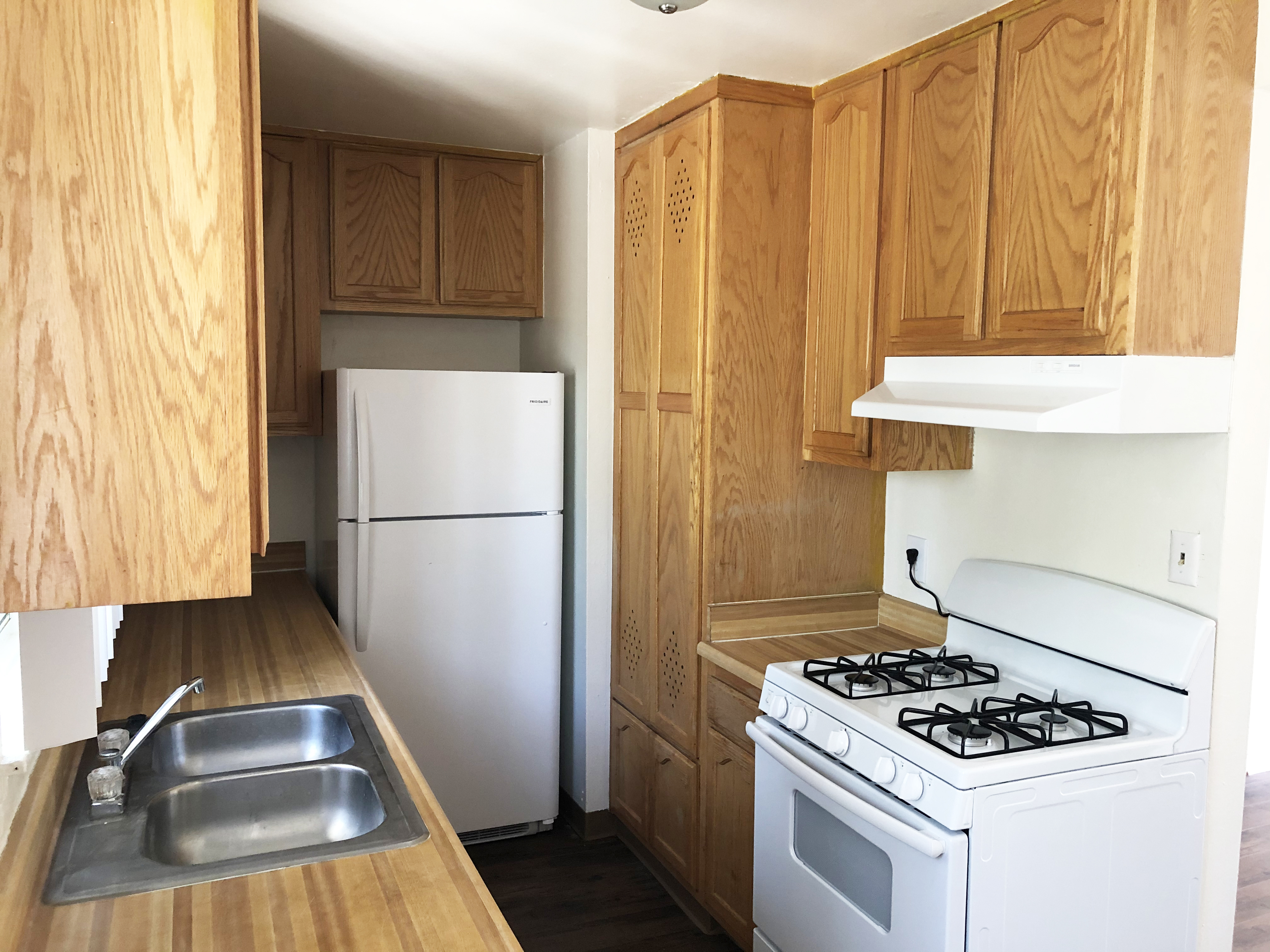 Interior view of a kitchen in a unit showing a stove, refrigerator, sink and cabinets.