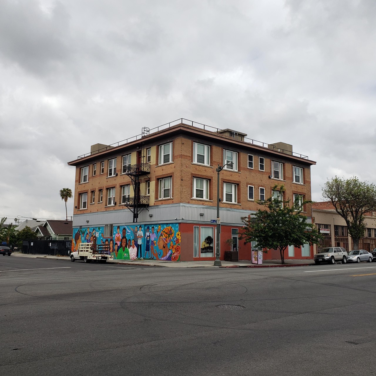 Corner street view of three story brick building with mural along one side of building.