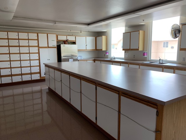 View of a kicthen area that shows two large counters counters and many cabinets. There is a refrigerator and a sink visible.