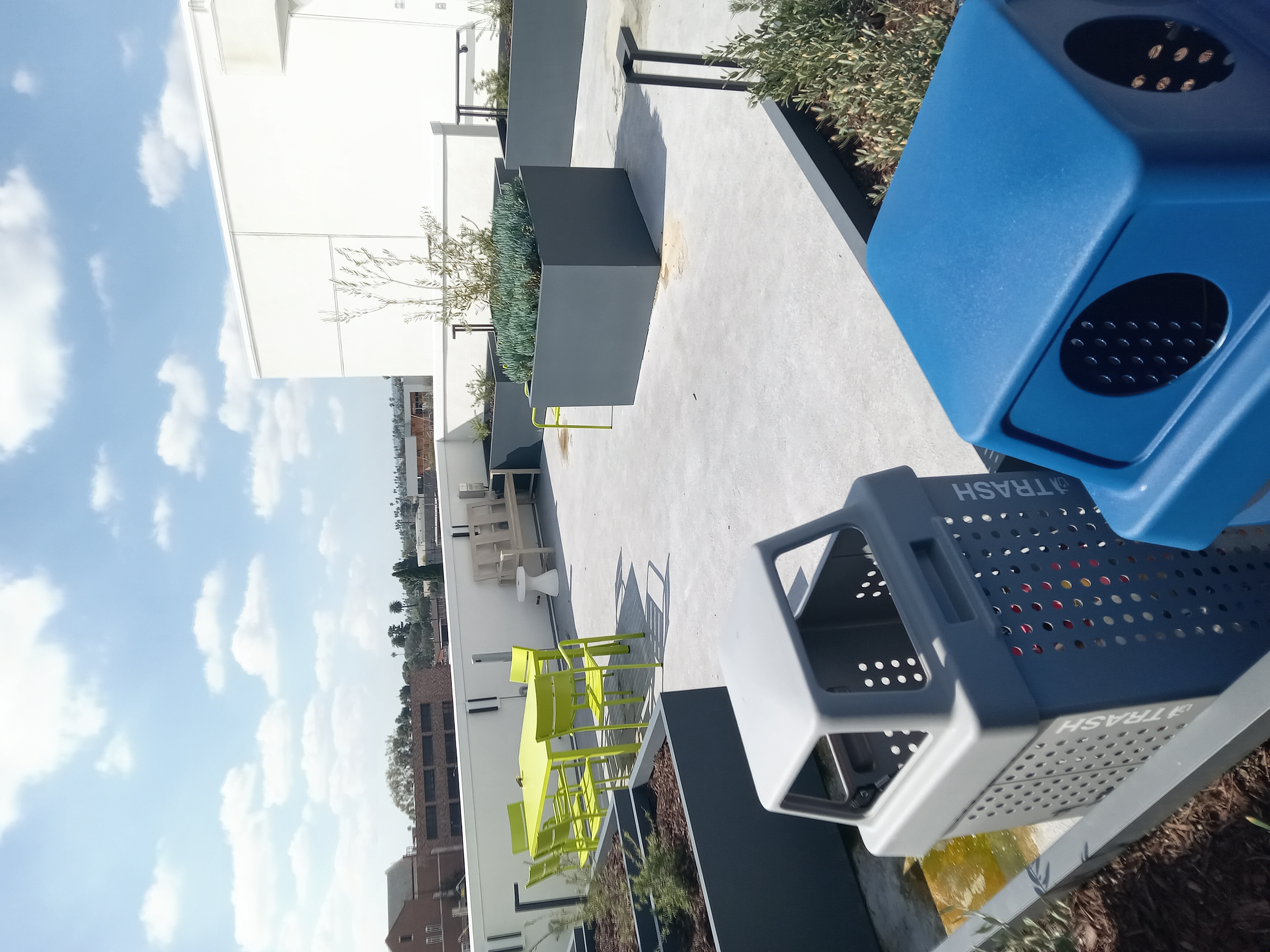 Rooftop: lime-green table and chairs, view of palms and hills, scattered planters with shrubs and succulents, trash and recycling