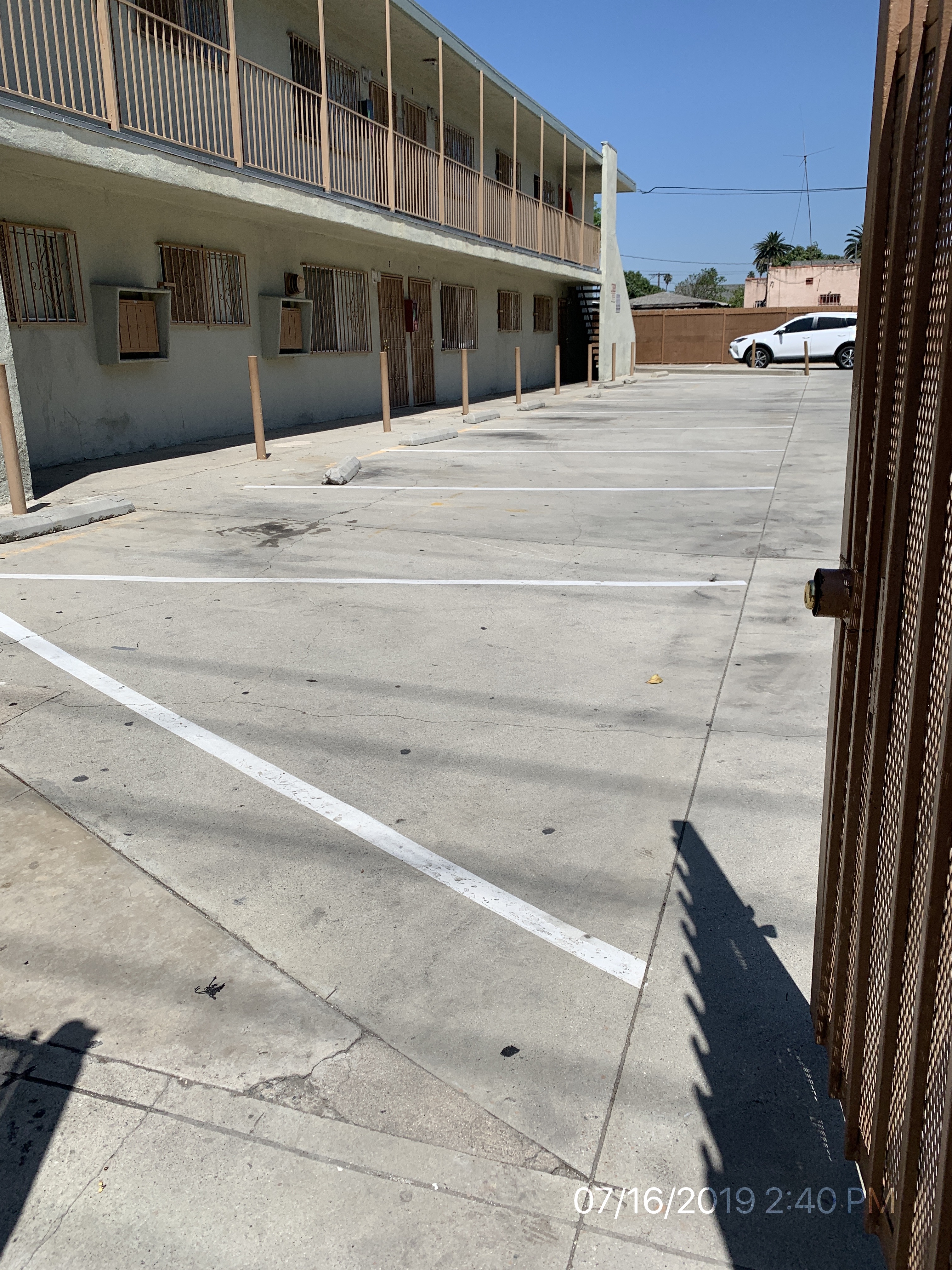 View of an outdoor parking lot of a two story building. Mailboxes are located on this side, and there is a staircase that leads upstairs.