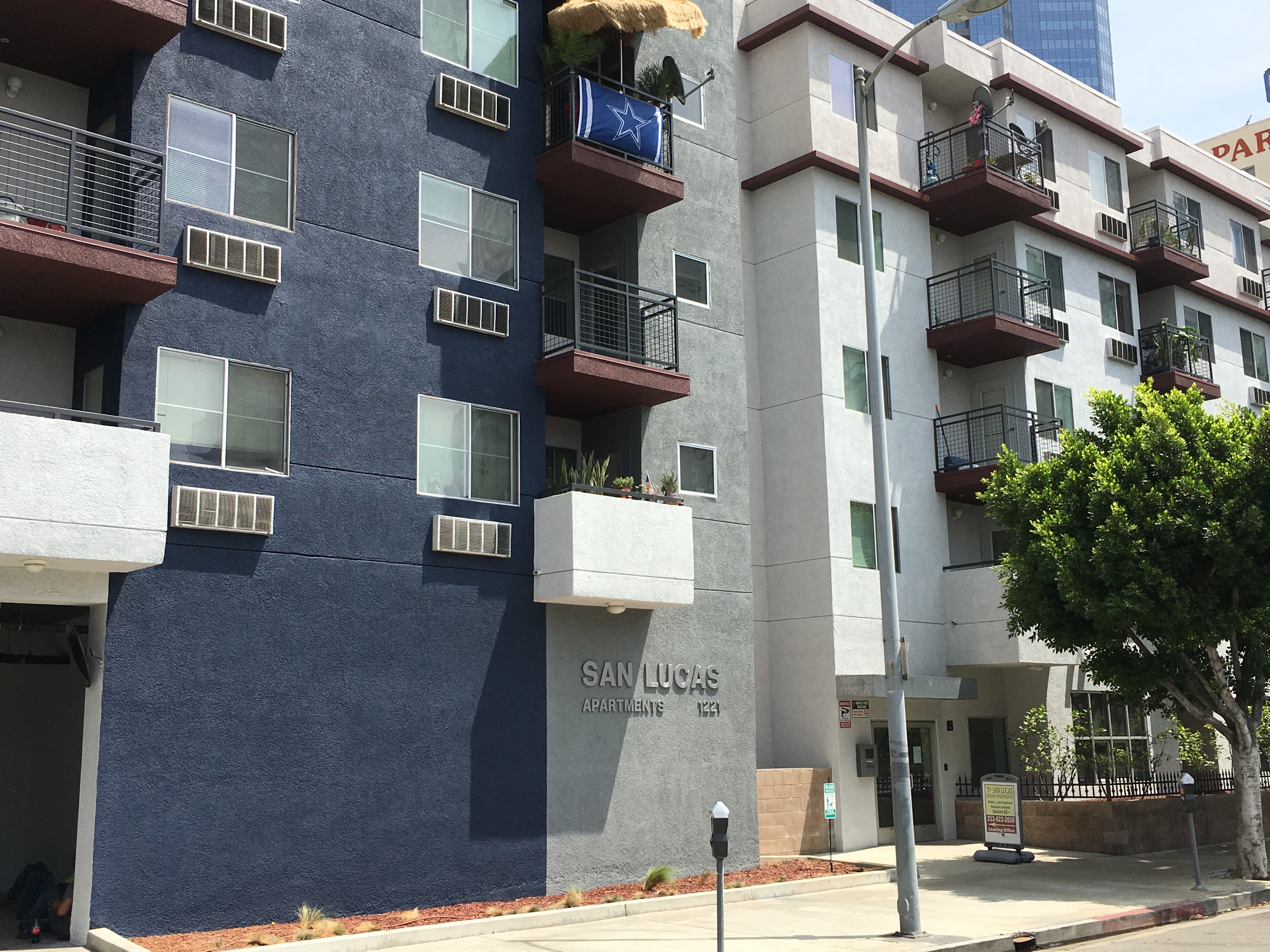 Street view of San Lucas Apartments, 5 story grey and blue building with balconies and lamp post in front