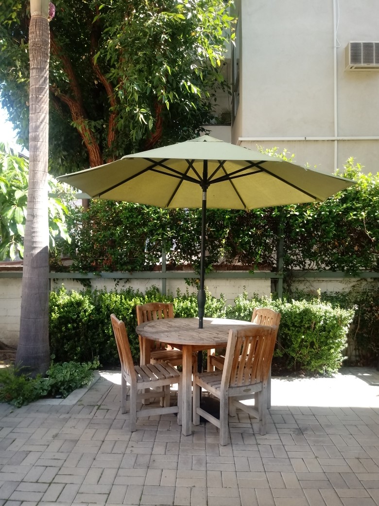 Alexandria House court yard. Patio table and four chairs with umbrella for shade. bushes located along wall