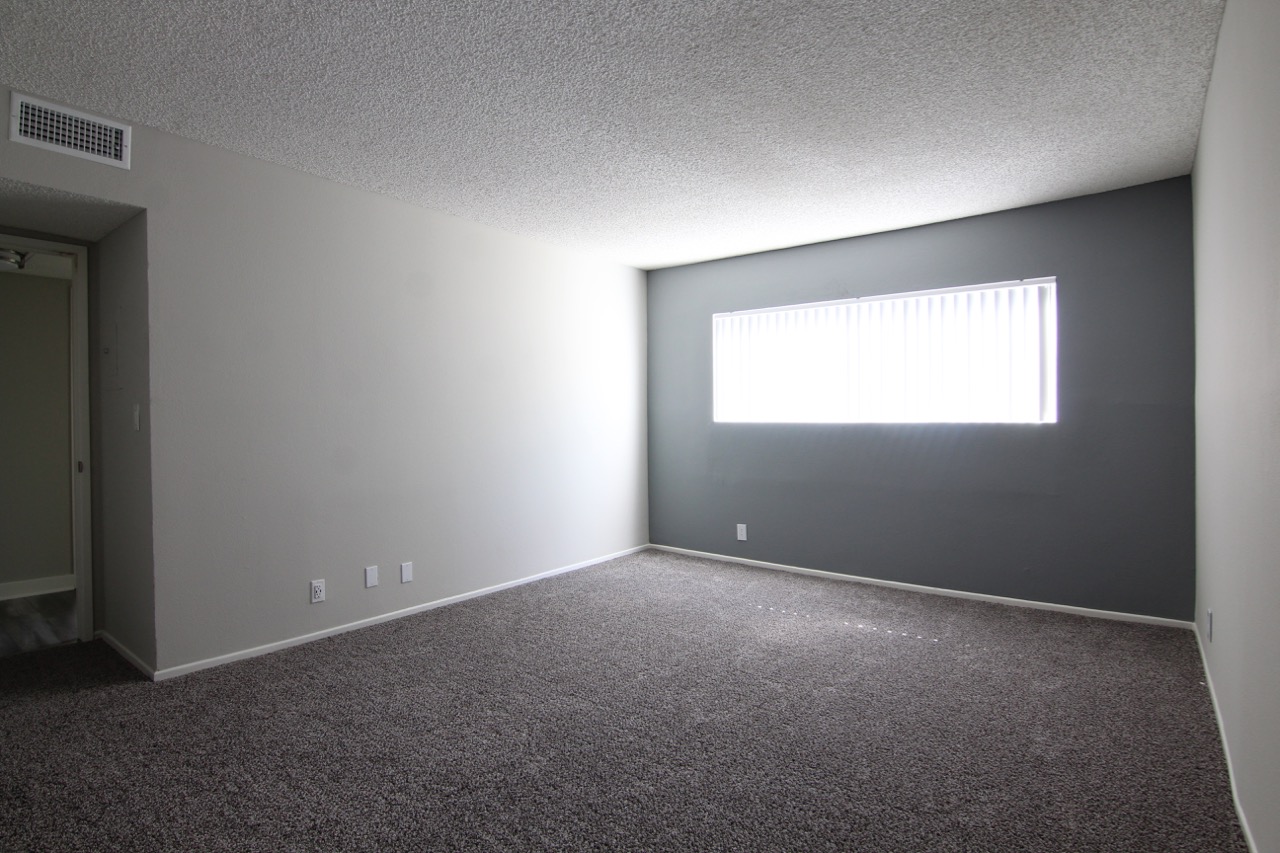Bedroom with carpeted flooring. There is a wide window with blinds.