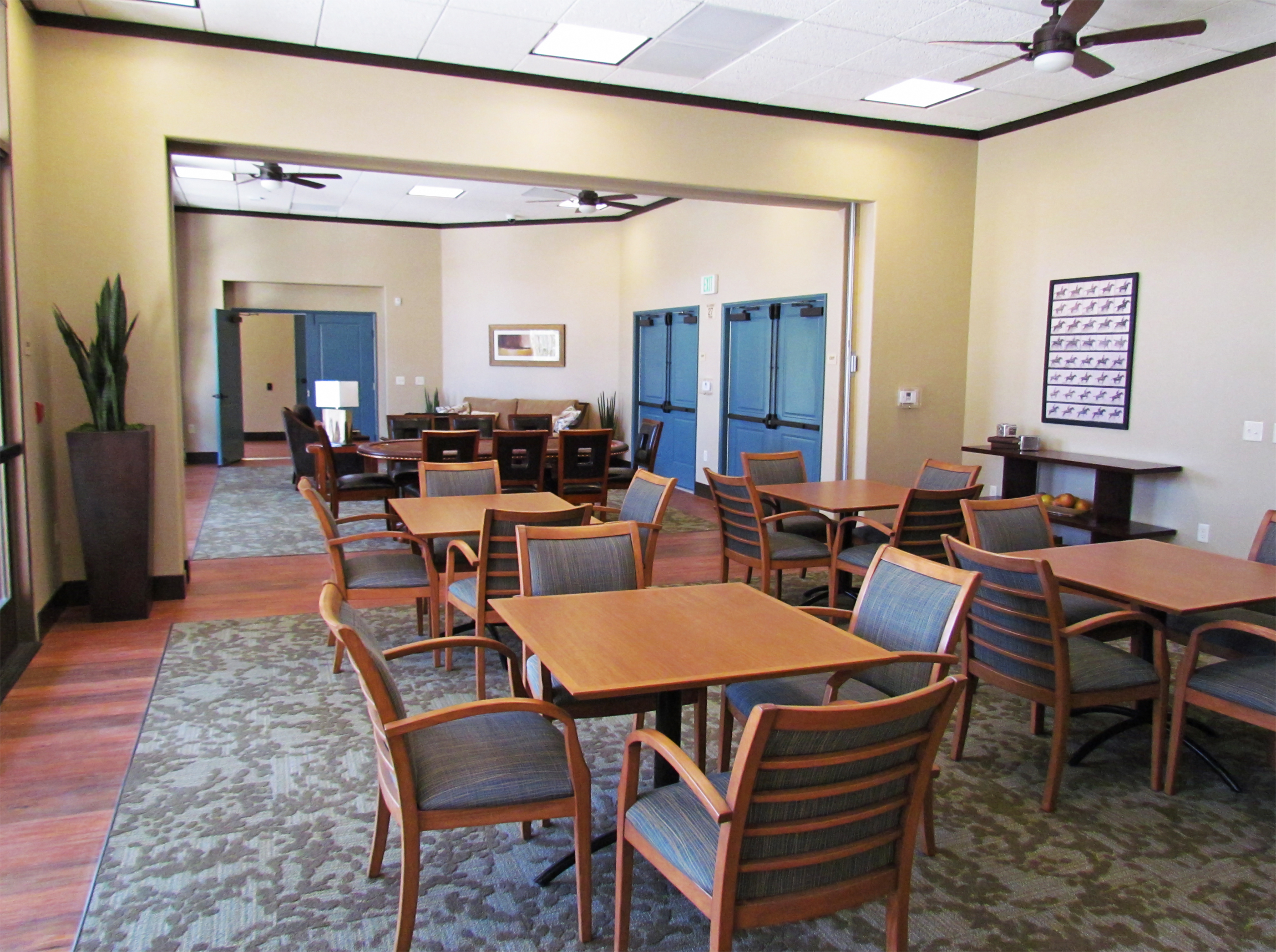 Interior view of a clubhouse at Osborne Street Apartments. 4 square tables and chairs and long oval table with chairs