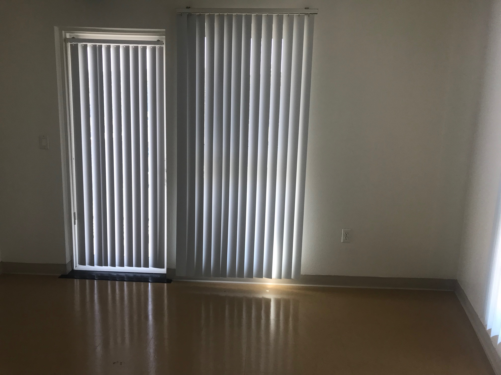 Interior view of a bedroom. Floors are tiled and there are two large horizontal blinds covering two windows.