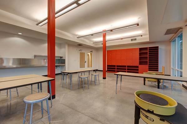 Community Room. Large open area with tables and stools. Tall wide orange book shelf along back wall. Two weightbearing pillars in the middle of the room.