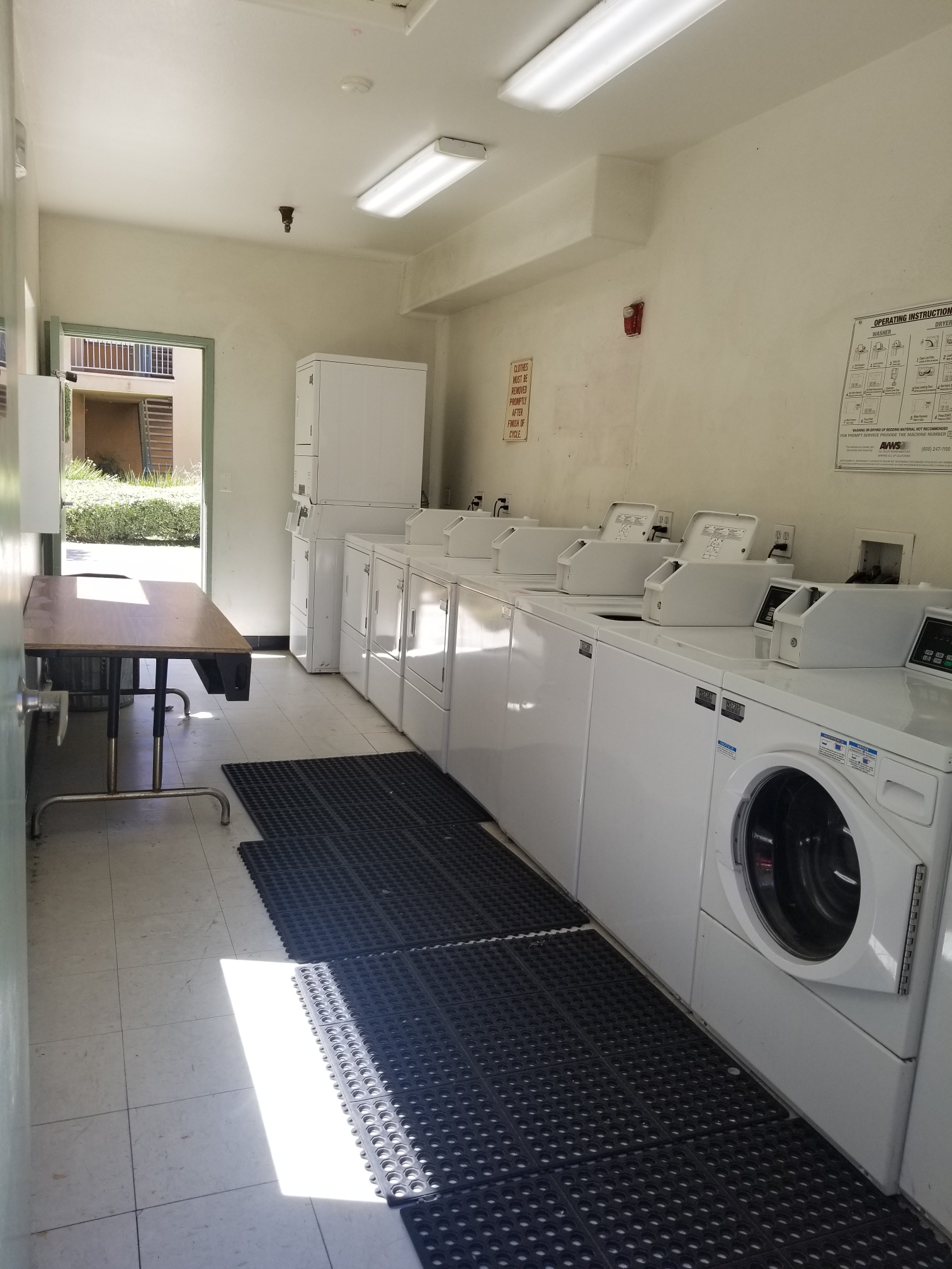 Willow Tree Village community laundry room. Side by side washer and dryers. Anti-slip mats. Long table located near entrance of room