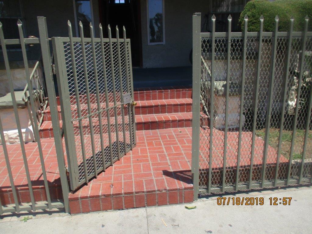 Front iron gate open door, brick entrance with two steps and handrails, green and white wide colums on each side of the entrance with bushes on them.