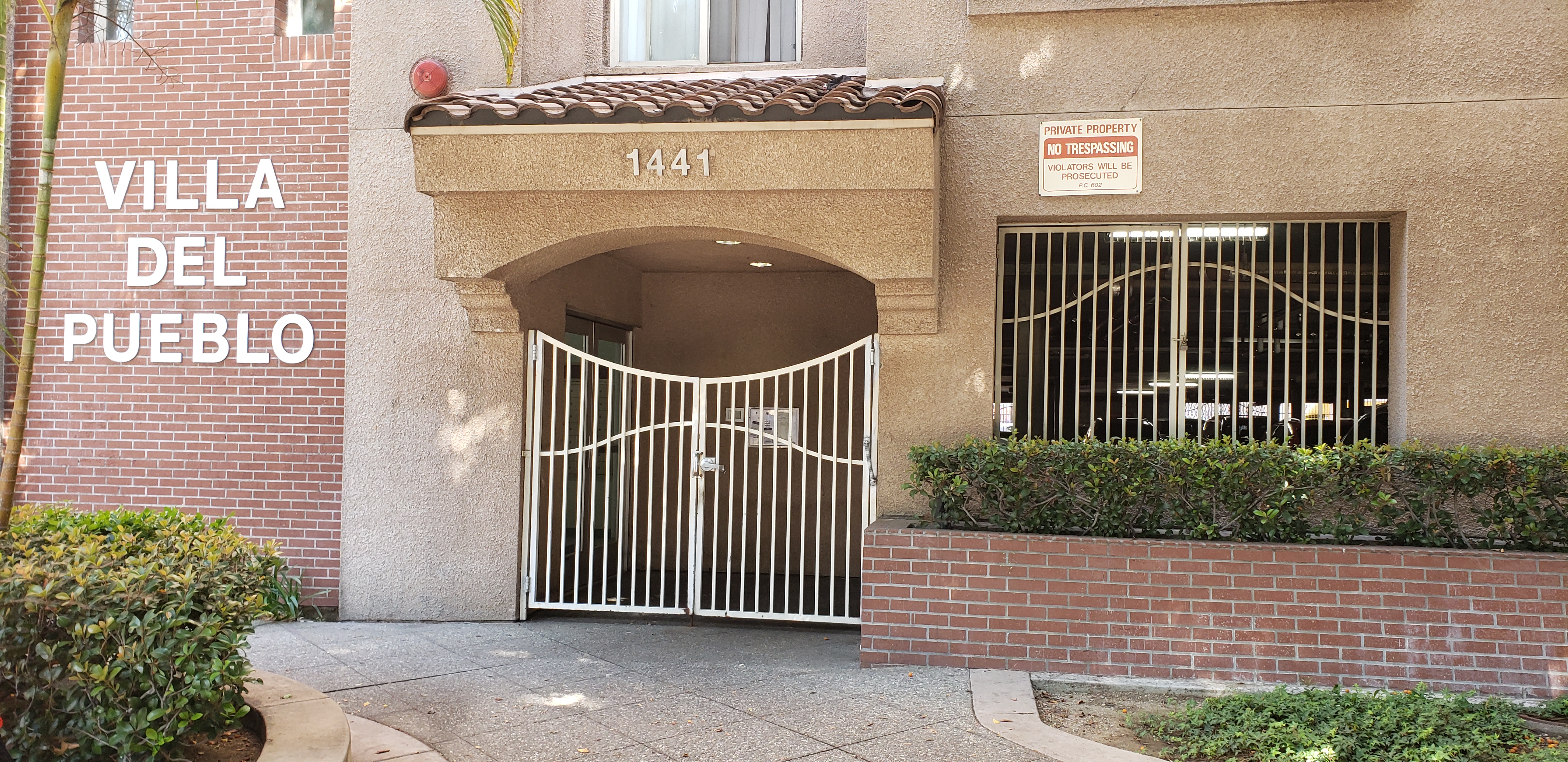Front view of a gated entrance to a building. There are bushes aligned on the sides of the building. Entrance is ground level.