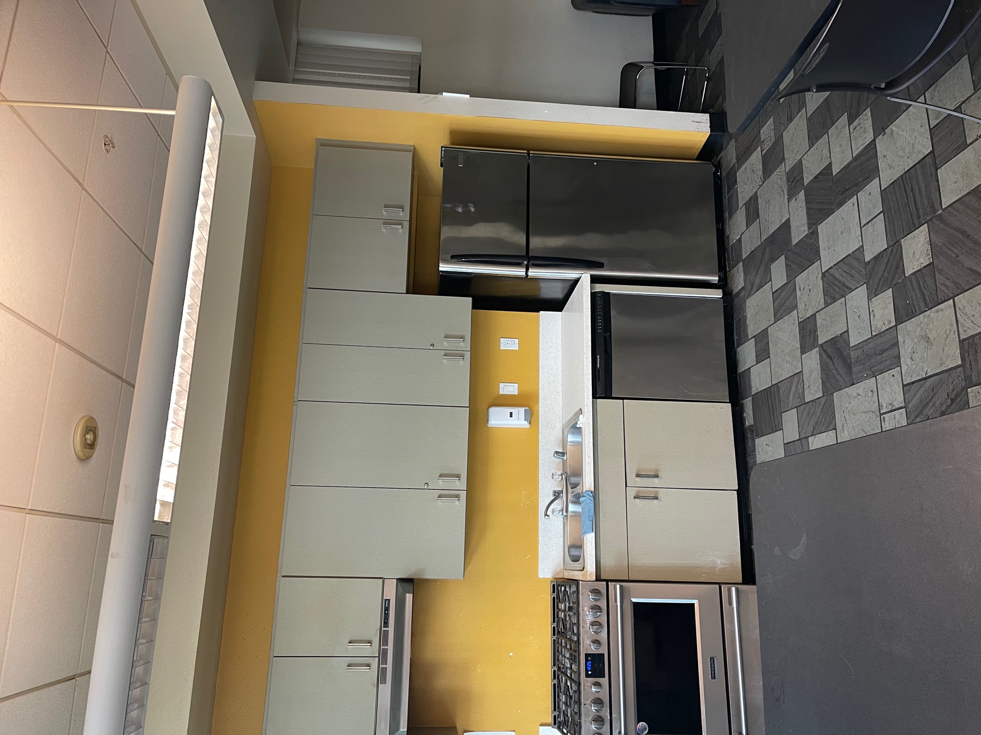 Photo of a room showing kitchen cabinets, a refrigerator, sink and a range.