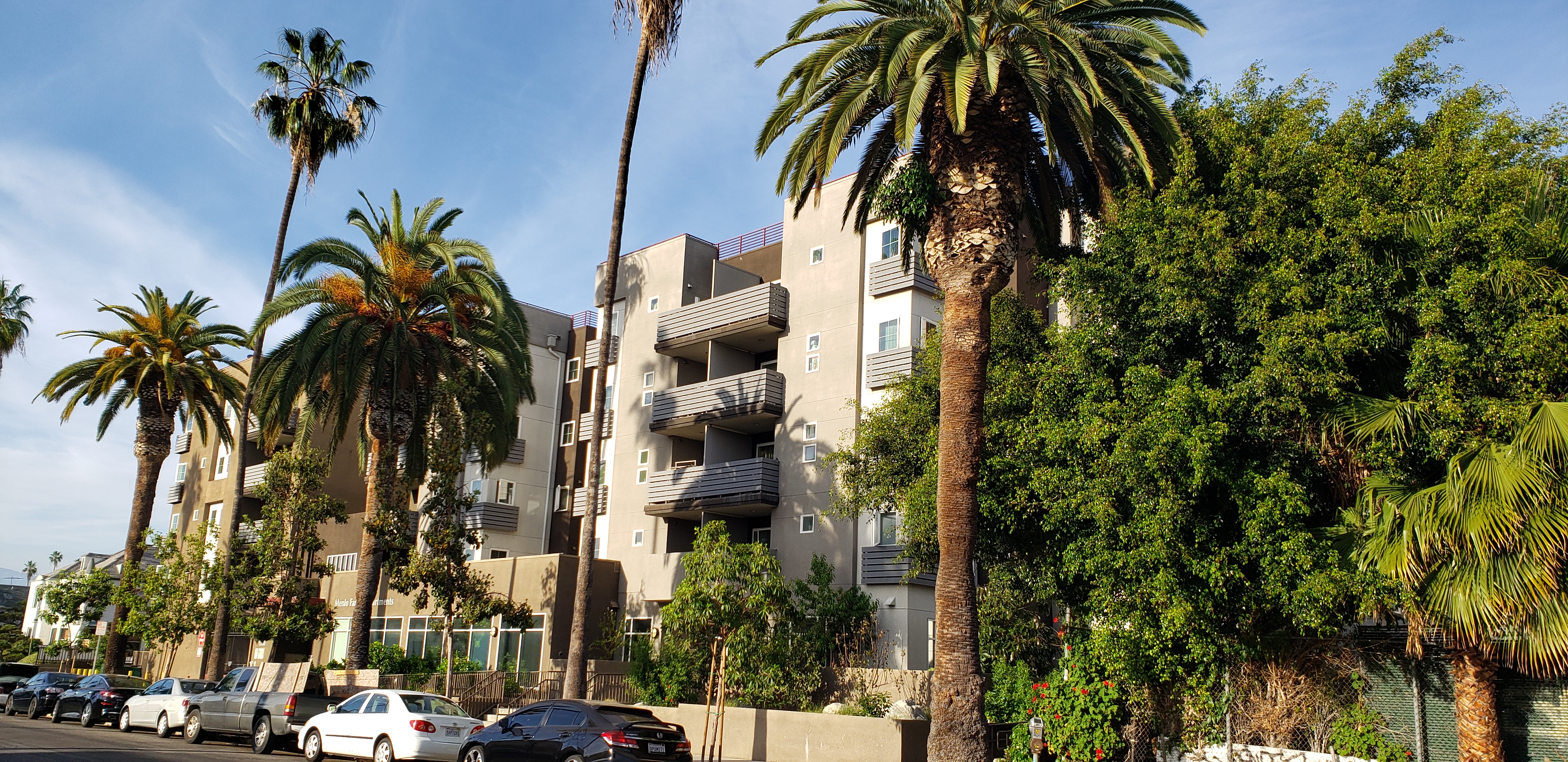 Street view of Menlo Family Housing with palm trees in front of building and cars parked along the street