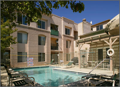 View of a gated swimming pool surrounded by the units, multiple lounge chairs, a White round lifesaver.
