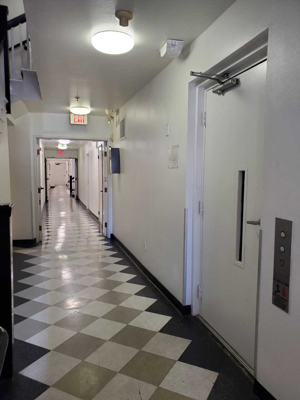 View of a large hallway on a ground floor. There is an elevator on on one side, and a stair case across from it.