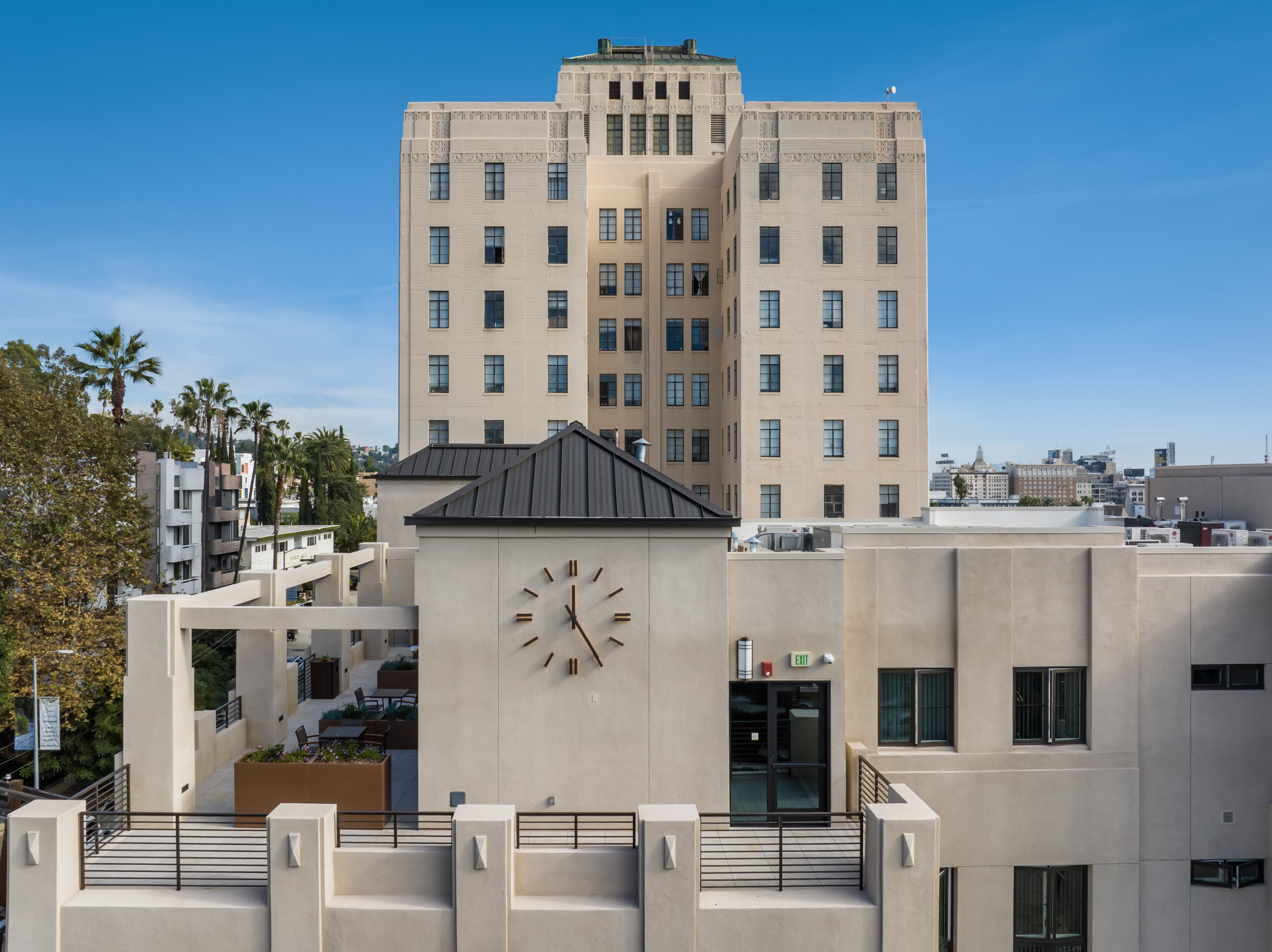 Contemporary building with a minimalist clock on its facade, surrounded by palm trees under a clear blue sky. Urban setting, calm atmosphere.
