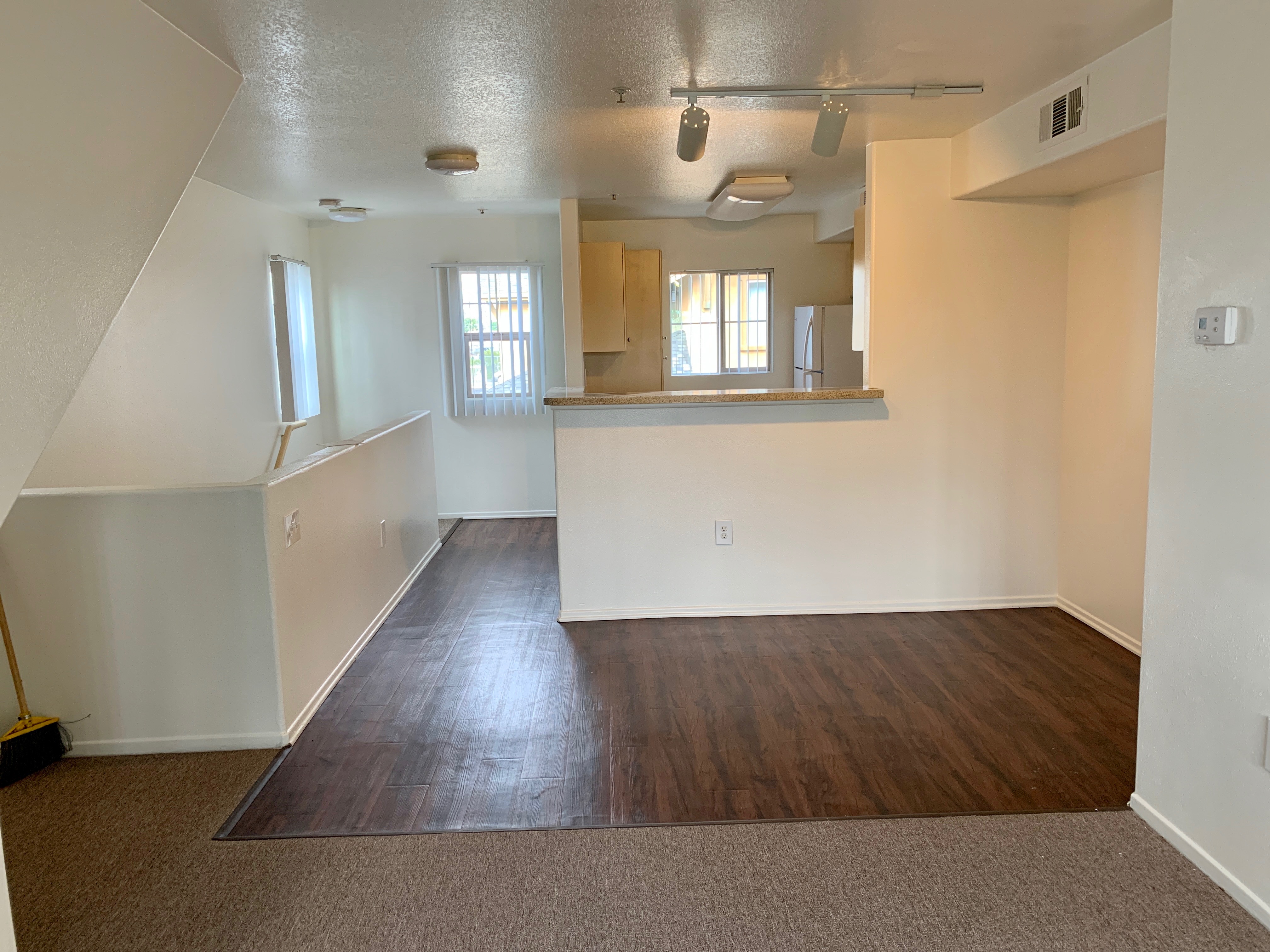 View of a vacant unit, half carpeted and other half linoleum, kitchen.