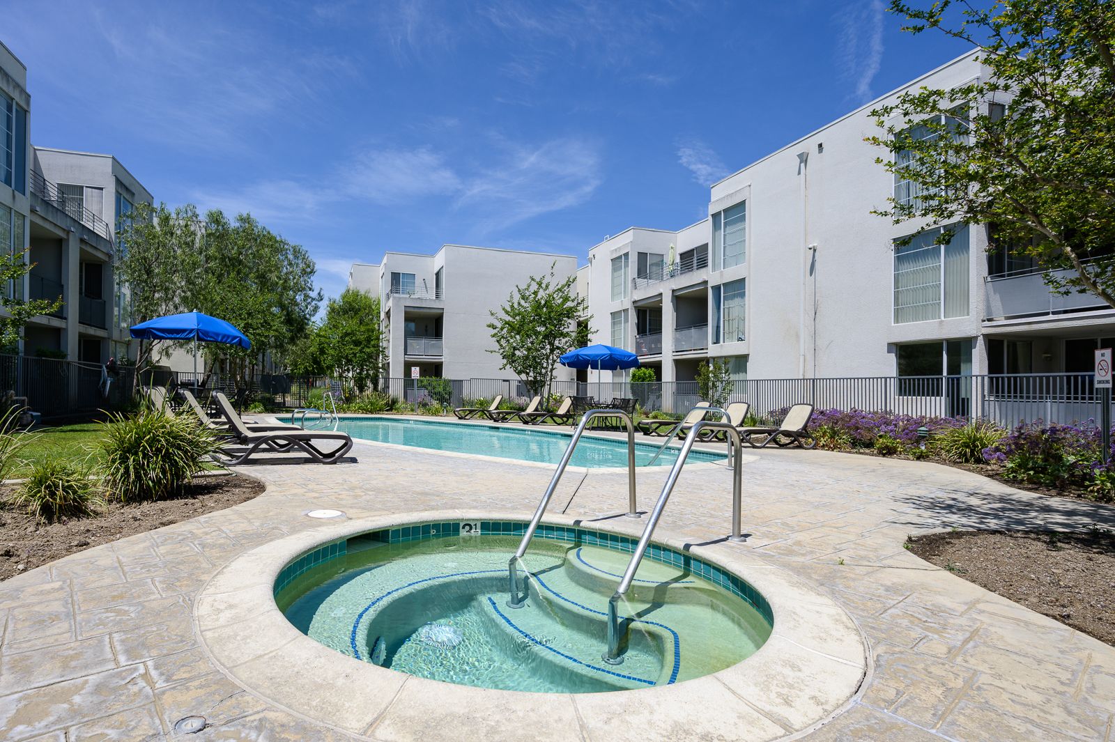 Gated pool area with twelve lounge chairs, two patio tables with umbrellas, and a 3.5 feet deep jacuzzi.