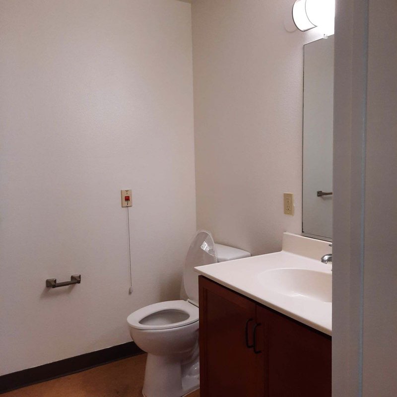 Photo of unit bathroom sink and toilet. Bathroom is painted white, toilet is while and countertop is white.