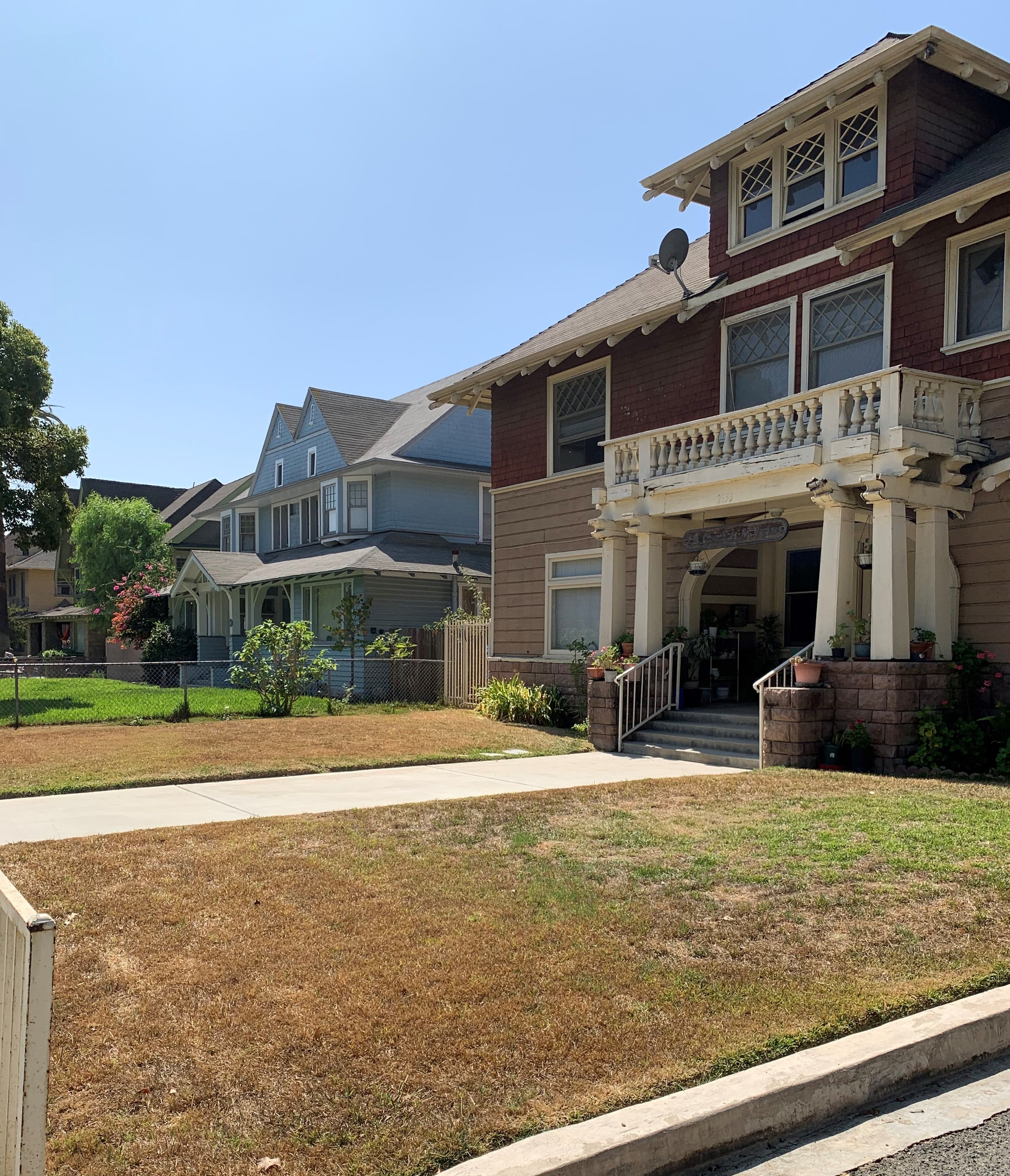 Front side view of a two story complex that resembles a house. The front area has grassand some plants. Entrance is accessed through a staircase with handle bars on both sides. Above the entrance, there is a balcony.