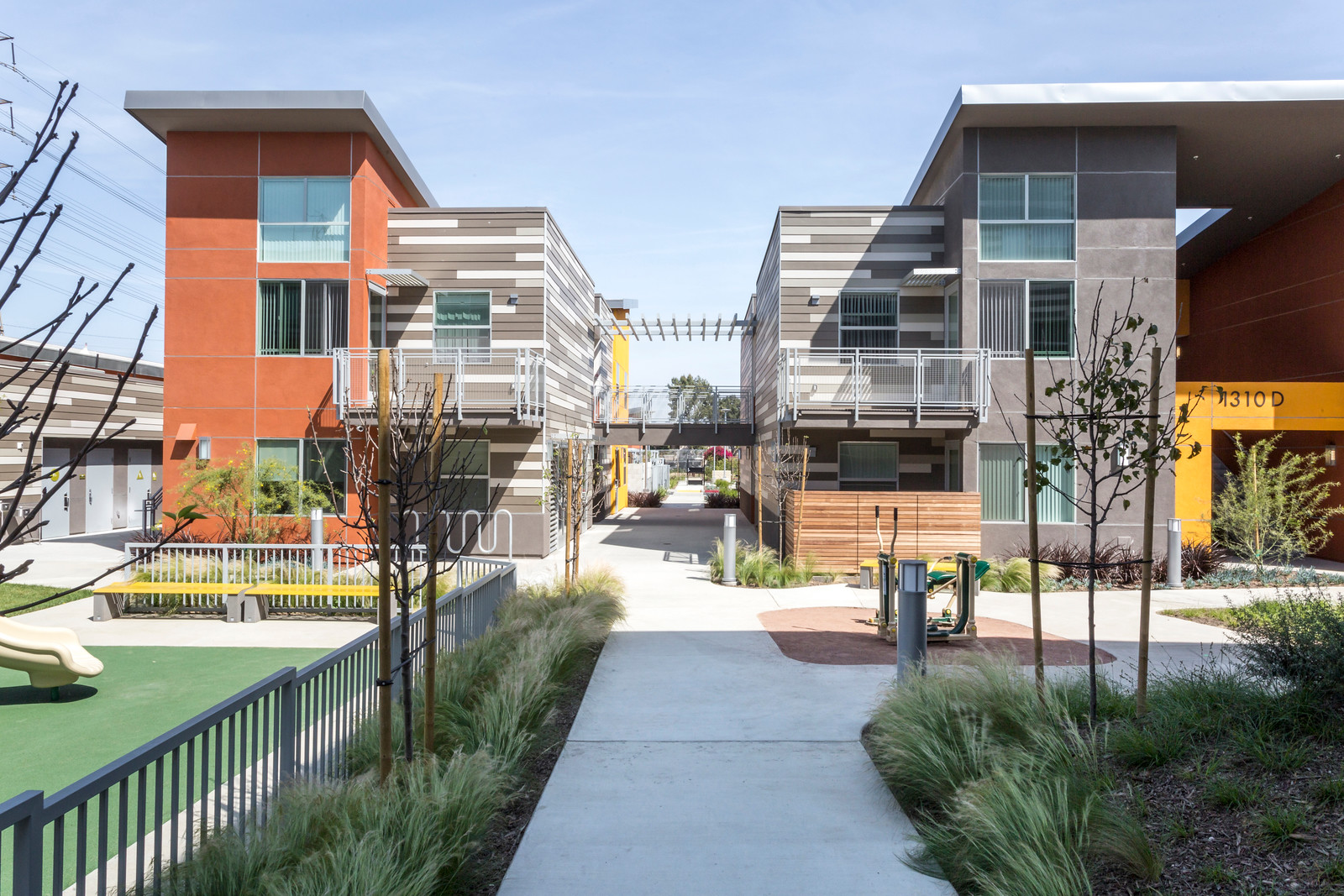 Exterior view of Sage Park Apartments community area. Paved walkways, landscaping, fenced in playgound with benches.